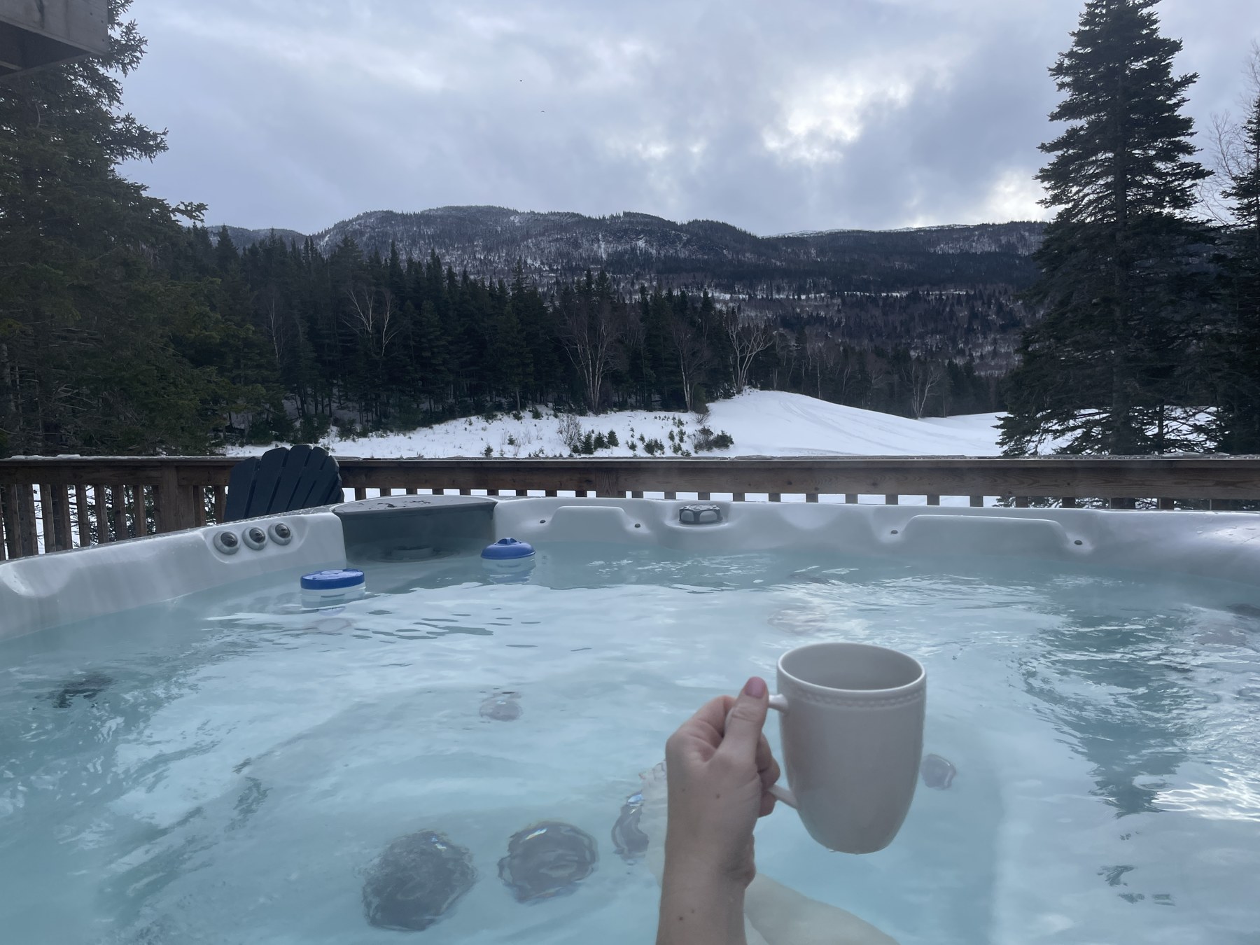 A coffee mug held in the hot tub overlooking the snowy Humber Valley