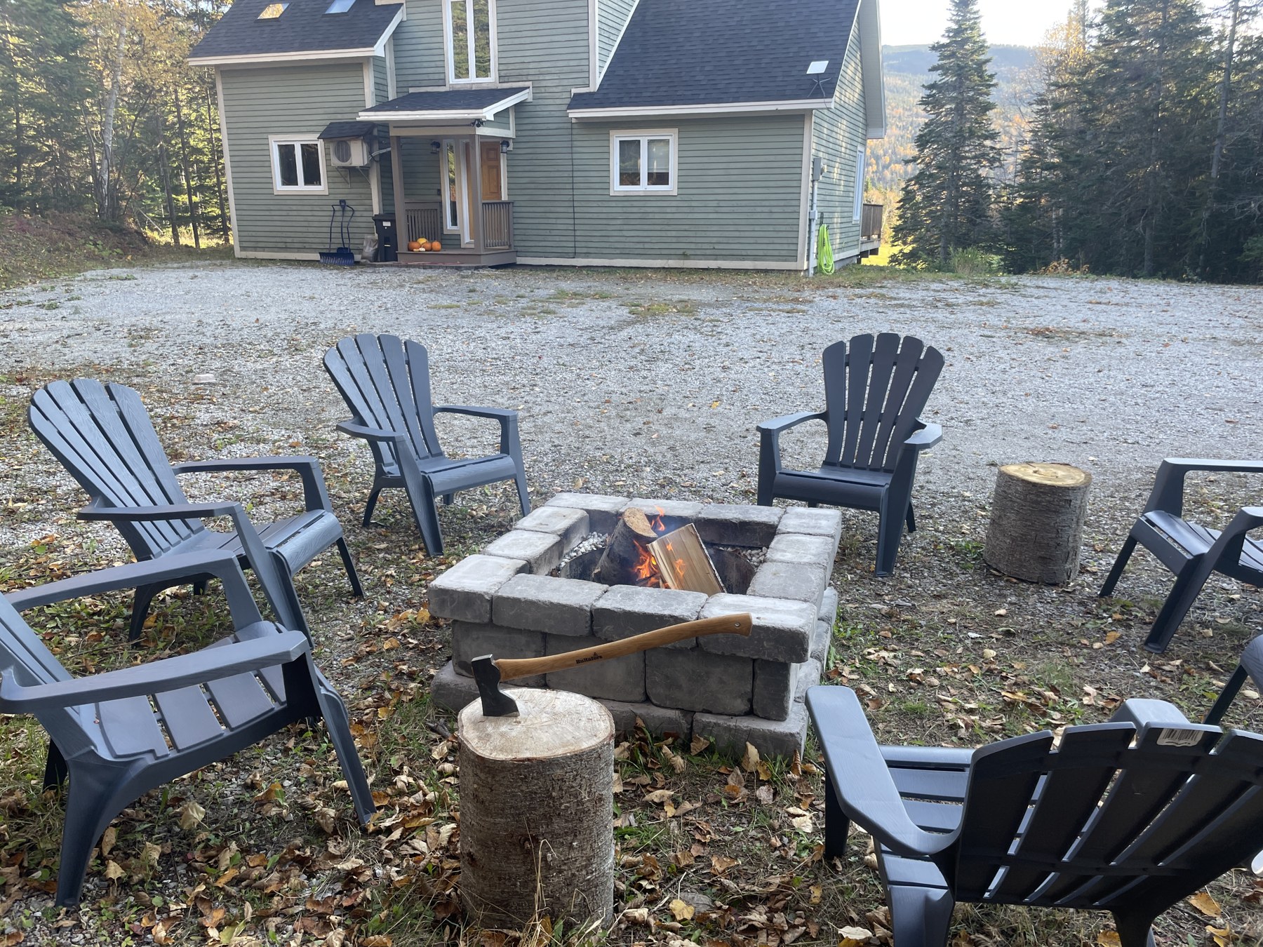 A glowing outdoor firepit surrounded by Adirondack chairs in front of Humber House